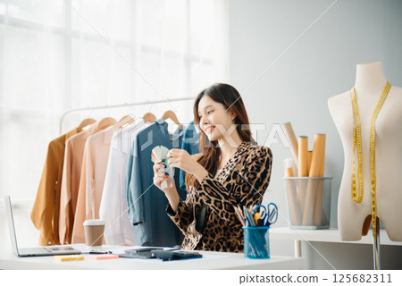 Asian young woman on desk in office of fashion designer and holds tablet, laptop and smartphone Asian young woman on desk in office of fashion designer and holds tablet, laptop and smartphone 125682311
