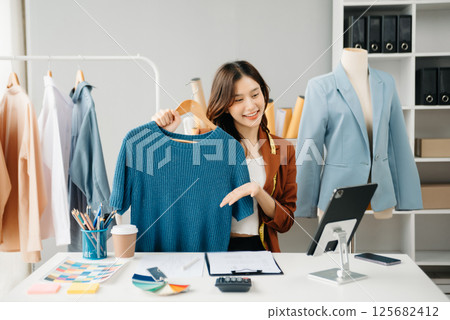 Fashion blogger concept, Young Asian women selling clothes on video streaming.Startup small business SME, using smartphone or tablet taking receive 125682412