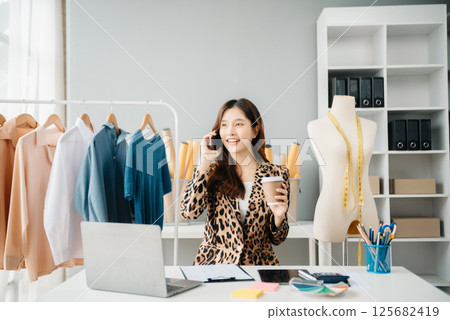 Asian young woman on desk in office of fashion designer and holds tablet, laptop and smartphone 125682419