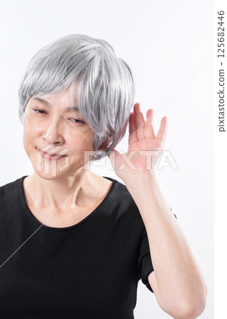An elderly woman smiling and listening with her hand over her ear An elderly woman smiling and listening with her hand over her ear 125682446