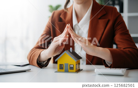 Female real estate agent is use hands to protect red roof for the concept of real estate investment about house trading, purchase at desk in office Female real estate agent is use hands to protect red roof for the concept of real estate investment about house trading, purchase at desk in office 125682501