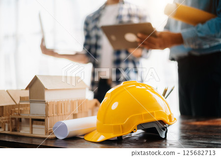 Engineer desk with object paper and tablet with blurry engineer teamwork hardworking to consults about their building project. Engineer desk with object paper and tablet with blurry engineer teamwork hardworking to consults about their building project. 125682713