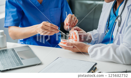 Dentist sitting at table with jaw samples tooth model and working with tablet and laptop in dental office professional dental clinic. medical doctor working 125682732