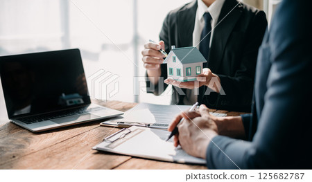 Real estate broker agent presenting and consult to customer to decision making sign insurance form agreement, home model, concerning mortgage loan offer in office 125682787