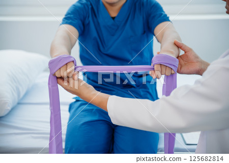 Physiotherapist Helping Patient While Stretching His Leg in bed in clinic 125682814