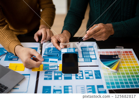 UX developer and ui designer brainstorming about mobile app interface wireframe design with customer breif and color code at modern office. UX developer and ui designer brainstorming about mobile app interface wireframe design with customer breif and color code at modern office. 125682817