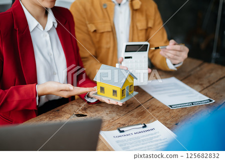 Buying a home or insurance deal, an insurance agent pointing a pen to those interested in renting a house, a contract, signing an Home buying agreement in office Buying a home or insurance deal, an insurance agent pointing a pen to those interested in renting a house, a contract, signing an Home buying agreement in office 125682832