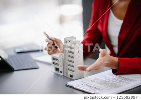 Real estate broker agent presenting and consult to customer to decision making sign insurance form agreement, home model, concerning mortgage loan offer in office Real estate broker agent presenting and consult to customer to decision making sign insurance form agreement, home model, concerning mortgage loan offer in office 125682887