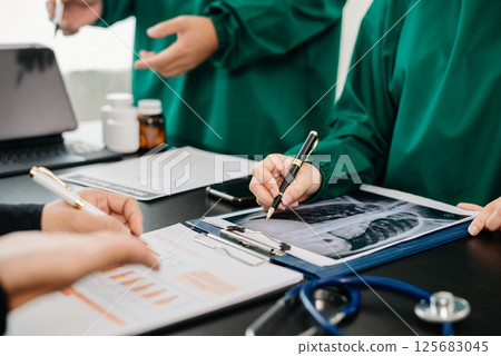 Medical team having a meeting with doctors in white lab coats and surgical scrubs seated at a table discussing a patients working online using computers in the medical 125683045