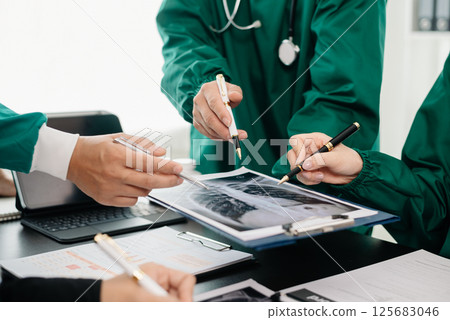 Medical team having a meeting with doctors in white lab coats and surgical scrubs seated at a table discussing a patients working online using computers in the medical Medical team having a meeting with doctors in white lab coats and surgical scrubs seated at a table discussing a patients working online using computers in the medical 125683046