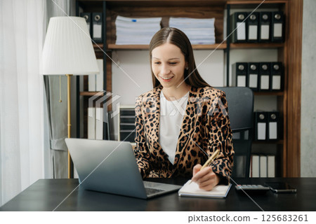 Beautiful woman using laptop and tablet while sitting at her working place. Concentrated at work. 125683261