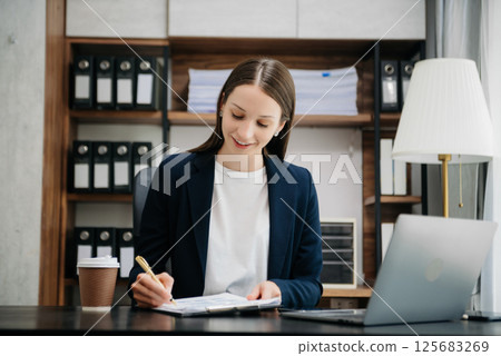 Beautiful woman using laptop and tablet while sitting at her working place. Concentrated at work. 125683269