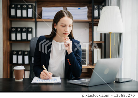 Beautiful woman using laptop and tablet while sitting at her working place. Concentrated at work. 125683270