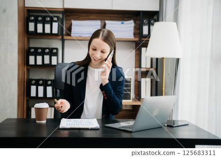 Beautiful woman using laptop and tablet while sitting at her working place. Concentrated at work. Beautiful woman using laptop and tablet while sitting at her working place. Concentrated at work. 125683311