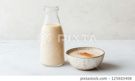 Oat milk in glass bottle and ceramic bowl with cinnamon on white background National Soy Foods Month 125683406