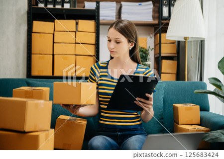 Caucasian young woman SME working using smartphone or tablet taking receive and checking online purchase shopping order to freelance online concept. Caucasian young woman SME working using smartphone or tablet taking receive and checking online purchase shopping order to freelance online concept. 125683424