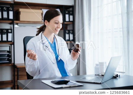 Attractive female doctor talking while explaining medical treatment to patient through a video call with laptop Attractive female doctor talking while explaining medical treatment to patient through a video call with laptop 125683661