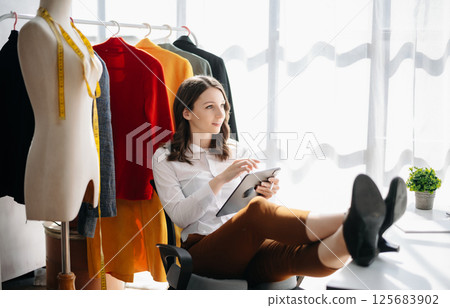 Fashion designer woman talking smart phone and using laptop with digital tablet computer in modern studio in morning light 125683902
