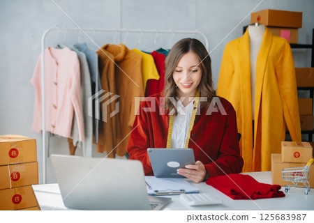 Fashion designer woman talking smart phone and using laptop with digital tablet computer in modern studio Fashion designer woman talking smart phone and using laptop with digital tablet computer in modern studio 125683987