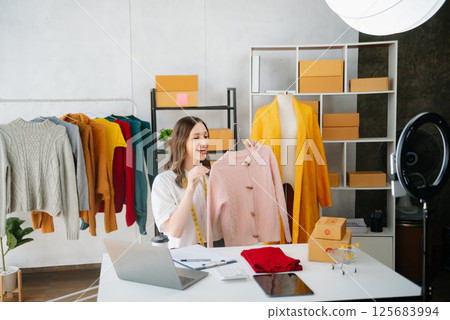 Beautiful lady blogger showing clothes in front of the camera to recording vlog video live streaming at her shop. Online Shopping Cart notion. 125683994