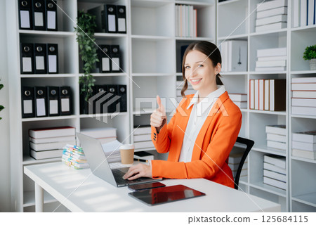 Confident business expert attractive smiling young woman typing laptop ang holding digital tablet on desk in creative office. 125684115