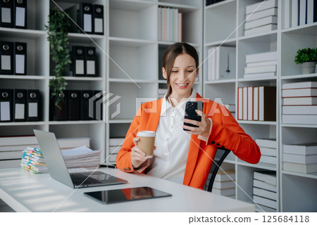 Confident business expert attractive smiling young woman typing laptop ang holding digital tablet on desk in creative office. 125684118