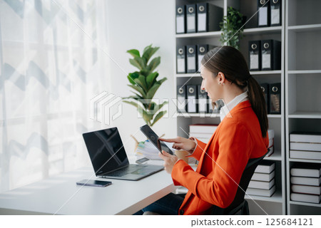 Confident business expert attractive smiling young woman typing laptop ang holding digital tablet on desk in creative office. Confident business expert attractive smiling young woman typing laptop ang holding digital tablet on desk in creative office. 125684121