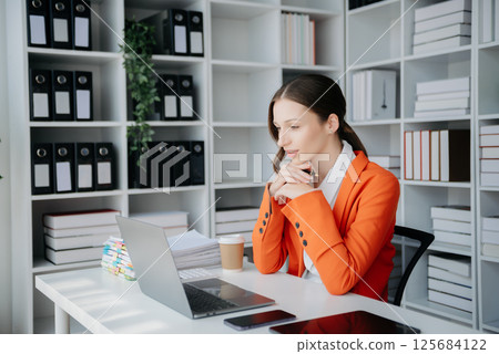 Confident business expert attractive smiling young woman typing laptop ang holding digital tablet on desk in creative office. Confident business expert attractive smiling young woman typing laptop ang holding digital tablet on desk in creative office. 125684122