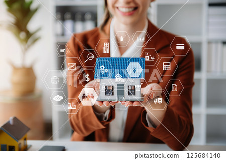 Young real estate agent worker working with laptop and tablet at table in office and small house beside it. 125684140