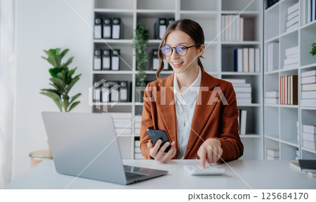 Confident business expert attractive smiling young woman typing laptop ang holding digital tablet on desk in creative office. Confident business expert attractive smiling young woman typing laptop ang holding digital tablet on desk in creative office. 125684170