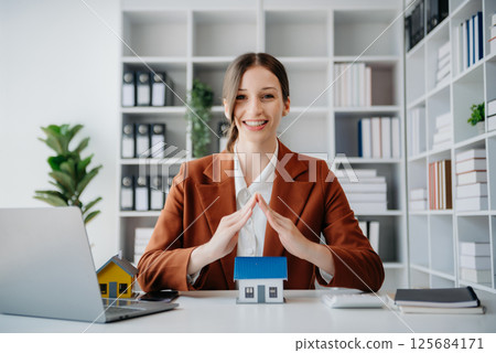 Female real estate agent is use hands to protect red roof for the concept of real estate investment about house trading, purchase at desk in office Female real estate agent is use hands to protect red roof for the concept of real estate investment about house trading, purchase at desk in office 125684171