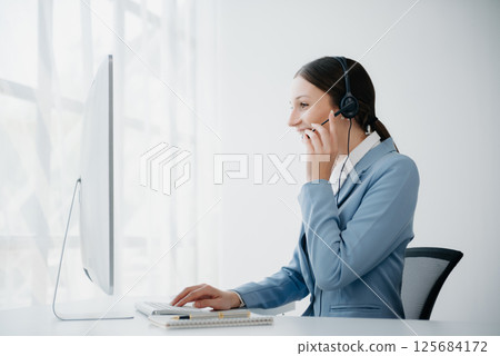Serious call center operator in wireless headset talking with customer, woman in headphones with microphone consulting client on phone in customer support service in business center Serious call center operator in wireless headset talking with customer, woman in headphones with microphone consulting client on phone in customer support service in business center 125684172