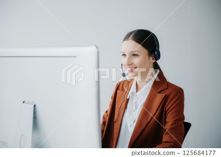 Serious call center operator in wireless headset talking with customer, woman in headphones with microphone consulting client on phone in customer support service in business center 125684177