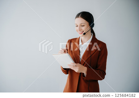 Serious call center operator in wireless headset talking with customer, woman in headphones with microphone consulting client on phone in customer support service in business center 125684182