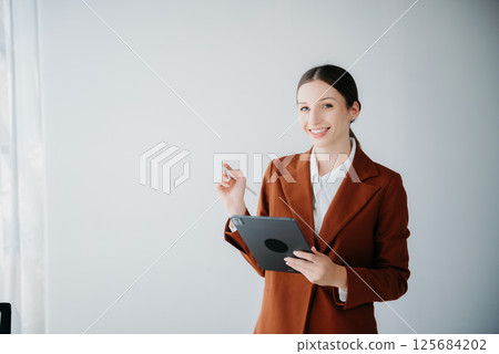 Smiling caucasian young businesswoman bank employee worker manager boss ceo looking at camera, using tablet, laptop and notepad online isolated background 125684202