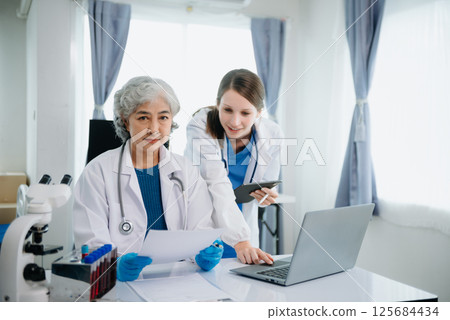 Hospital Ward. Doctor Talks With Professional Head Nurse or Surgeon, They Use Digital tablet Computer. Diverse Team of Health Care Specialists Discussing Test Result Hospital Ward. Doctor Talks With Professional Head Nurse or Surgeon, They Use Digital tablet Computer. Diverse Team of Health Care Specialists Discussing Test Result 125684434