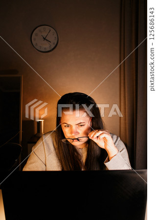 Woman working on computer late evening at home office. Concentrated female freelancer trying to solve business problems. Working and suffering from weariness. Woman working on computer late evening at home office. Concentrated female freelancer trying to solve business problems. Working and suffering from weariness. 125686143