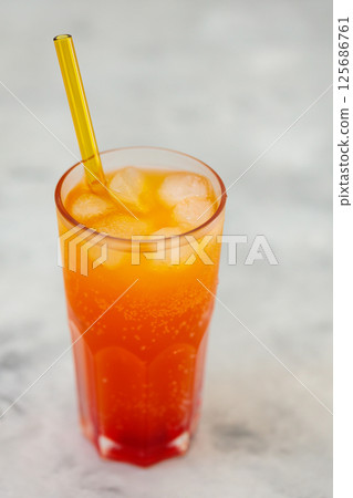 Refreshing Orange Carbonated Drink with Ice Cubes in Tall Glass on Gray Surface, Trendy Dirty Soda Concept 125686761