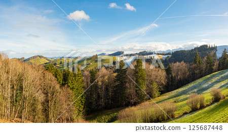 Mogelsberg, Switzerland - January 1st 2024: View over fields and forests towards snow coverd hills and mountains Mogelsberg, Switzerland - January 1st 2024: View over fields and forests towards snow coverd hills and mountains 125687448
