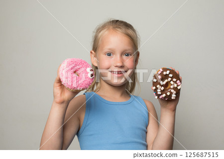 Funny child girl holding testy donut. Cute little girl with sweet food indoor 125687515