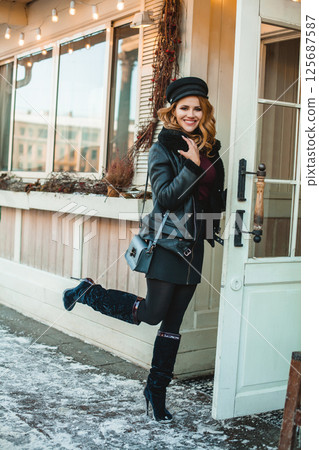 Smiling pretty brunette woman in black leather jacket and high heels with blue handbag standing  125687587