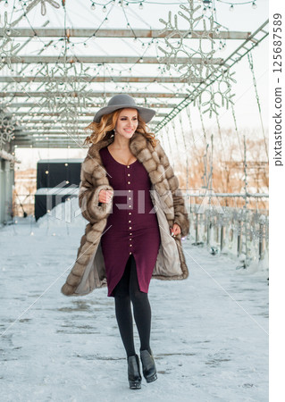 Beautiful woman walking out on city street background in cold outdoor wearing hat and fur coat 125687589