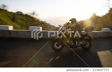 Driver riding motorcycle on empty asphalt road, blurred motiion, spring mountains 125687737