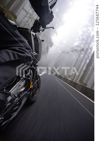 Driver riding motorcycle on empty road , back side view , foggy rainforest, spring mountains 125687744