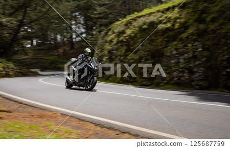Driver riding motorcycle on empty asphalt road, spring mountains 125687759