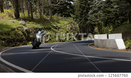 Driver riding motorcycle on empty asphalt road, spring mountains 125687760