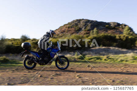Driver riding motorcycle on empty asphalt road, spring mountains Driver riding motorcycle on empty asphalt road, spring mountains 125687765