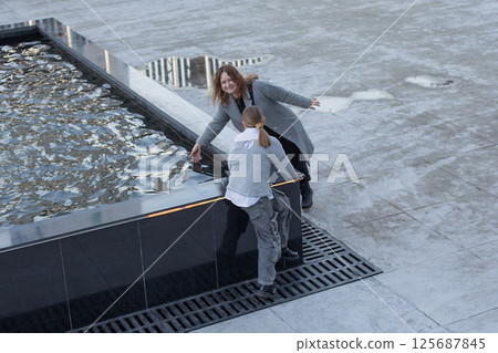 Positive woman and young girl child walking along the streets of the city. Childhood, happiness Positive woman and young girl child walking along the streets of the city. Childhood, happiness 125687845