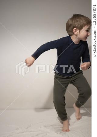 Young boy dancing on bed, having fun at home Young boy dancing on bed, having fun at home 125687871