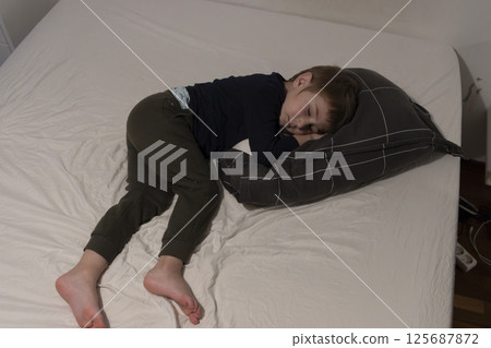 Young child sleeping soundly on a bed, hugging a pillow, enjoying a peaceful nap Young child sleeping soundly on a bed, hugging a pillow, enjoying a peaceful nap 125687872
